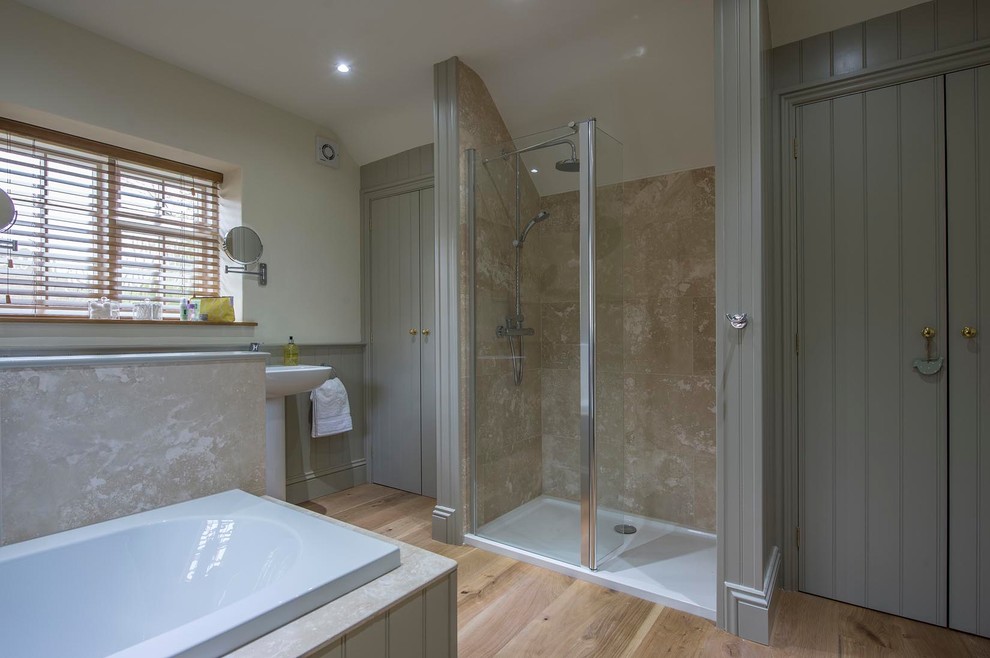 Photo of a large country kids bathroom in Other with grey cabinets, a drop-in tub, an open shower, a two-piece toilet, travertine, grey walls, light hardwood floors, a pedestal sink, brown floor and a hinged shower door.