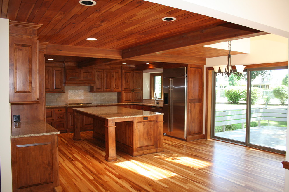 Example of a mountain style u-shaped light wood floor kitchen design in Milwaukee with raised-panel cabinets, light wood cabinets, granite countertops, beige backsplash, stone tile backsplash, stainless steel appliances and an island