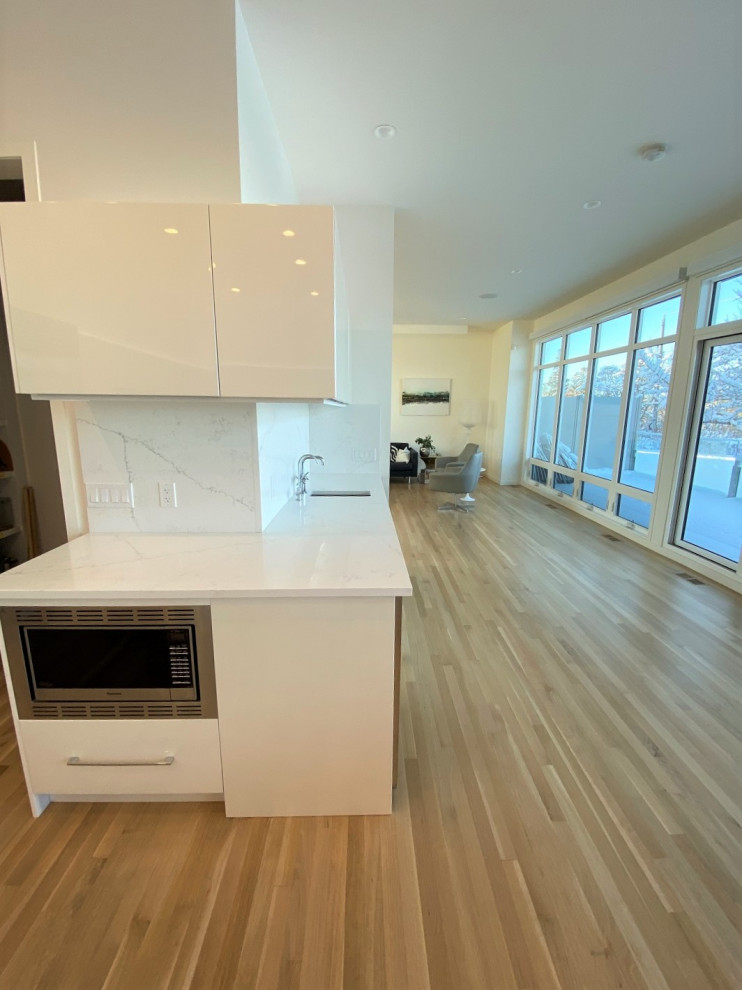 Large modern l-shaped eat-in kitchen in Calgary with an undermount sink, flat-panel cabinets, white cabinets, white splashback, stainless steel appliances, with island and white benchtop.