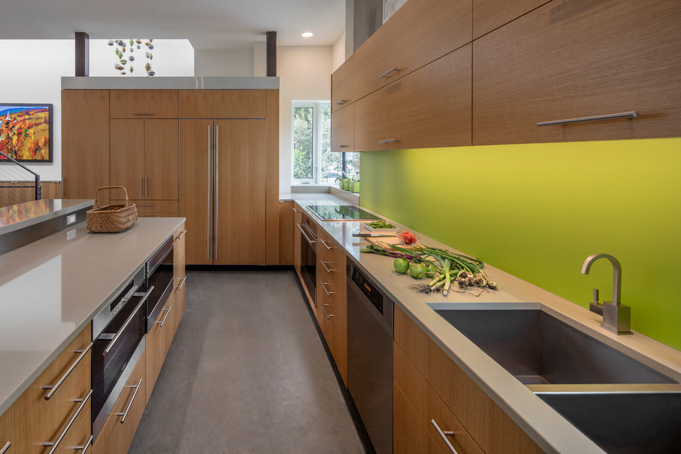 Inspiration for a modern l-shaped open plan kitchen in Phoenix with with island, flat-panel cabinets, light wood cabinets, green splashback, panelled appliances, a double-bowl sink, concrete floors and grey floor.