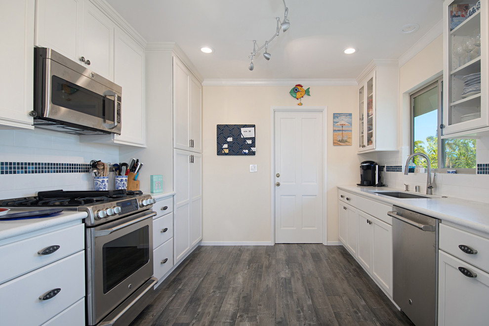 Large beach style u-shaped eat-in kitchen in San Diego with a drop-in sink, recessed-panel cabinets, white cabinets, granite benchtops, white splashback, subway tile splashback, stainless steel appliances, medium hardwood floors, a peninsula and brown floor.