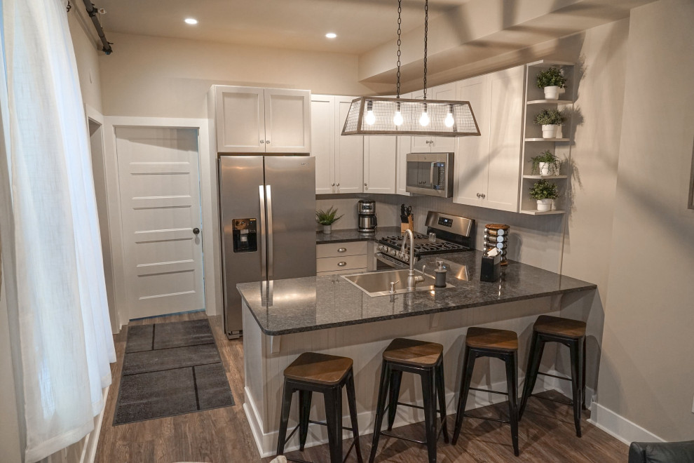 Small u-shaped eat-in kitchen photo with a drop-in sink, shaker cabinets, granite countertops, beige backsplash, stainless steel appliances and black countertops