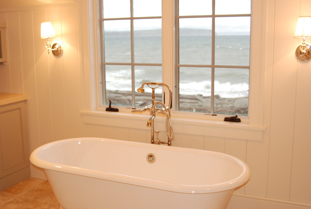 This is an example of a large beach style bathroom in Seattle with a claw-foot tub, white walls, beige cabinets, limestone benchtops, beige tile, stone tile and limestone floors.