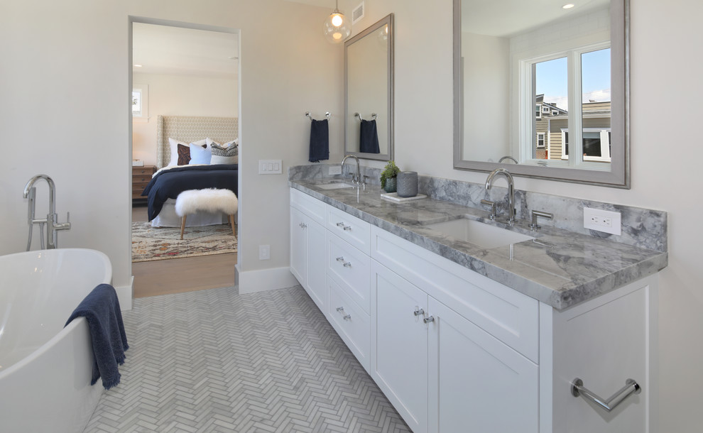 This is an example of a mid-sized beach style master bathroom in Orange County with shaker cabinets, white cabinets, a freestanding tub, a corner shower, white tile, subway tile, grey walls, marble floors, an undermount sink, marble benchtops, grey floor, a hinged shower door and grey benchtops.