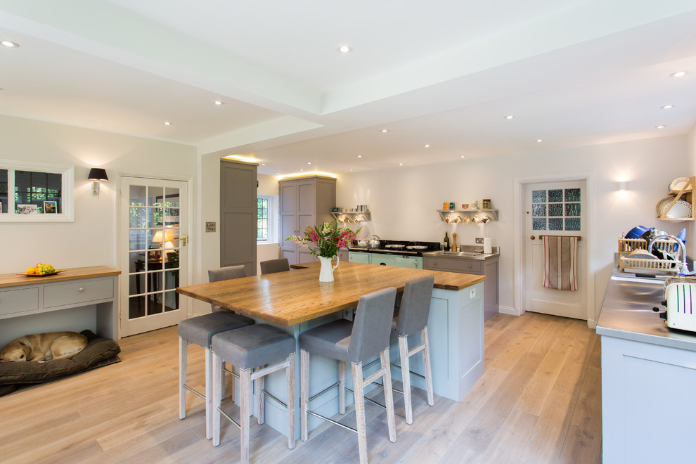 This is an example of a large country u-shaped eat-in kitchen in London with a farmhouse sink, shaker cabinets, grey cabinets, stainless steel benchtops, medium hardwood floors, with island and coloured appliances.