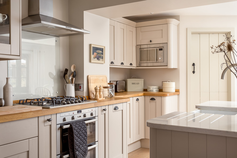 Inspiration for a large country galley open plan kitchen in Gloucestershire with an undermount sink, recessed-panel cabinets, beige cabinets, wood benchtops, stainless steel appliances, with island, brown floor and brown benchtop.