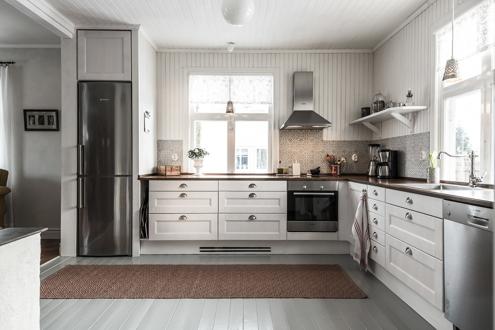 Photo of a large country l-shaped separate kitchen in Other with a drop-in sink, recessed-panel cabinets, white cabinets, wood benchtops, multi-coloured splashback, stainless steel appliances, painted wood floors and no island.