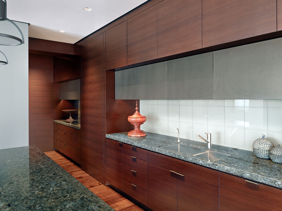 This is an example of a modern kitchen in San Francisco with an undermount sink, flat-panel cabinets, dark wood cabinets, white splashback, glass tile splashback and granite benchtops.