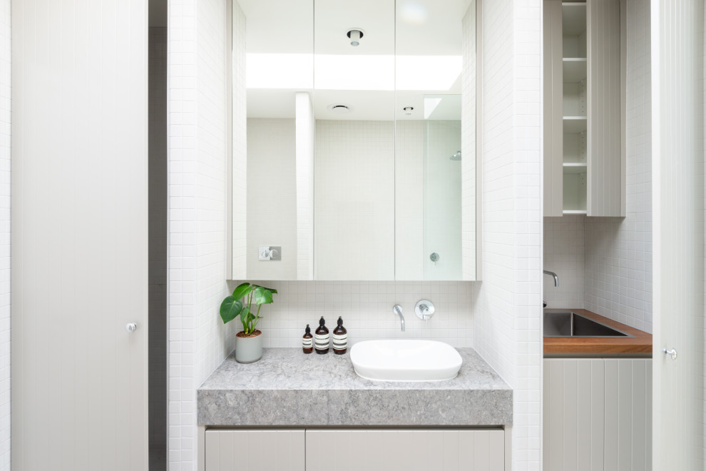 This is an example of a small scandinavian kids bathroom in Melbourne with flat-panel cabinets, grey cabinets, a drop-in tub, a shower/bathtub combo, a wall-mount toilet, white tile, porcelain tile, white walls, porcelain floors, a drop-in sink, granite benchtops, white floor, an open shower, grey benchtops, a laundry, a single vanity and a built-in vanity.