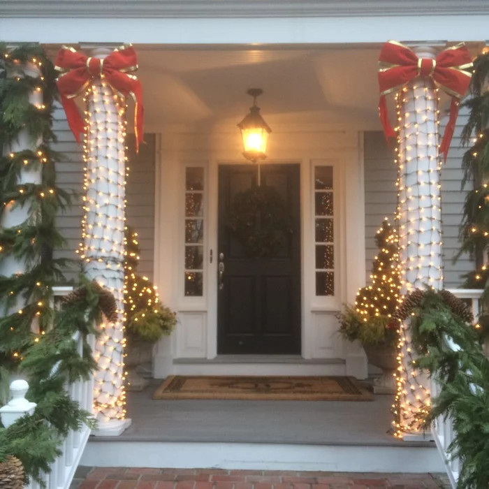White Pillars wrapped in Clear Lights with Green Garland and Large Gold lined Red Bows