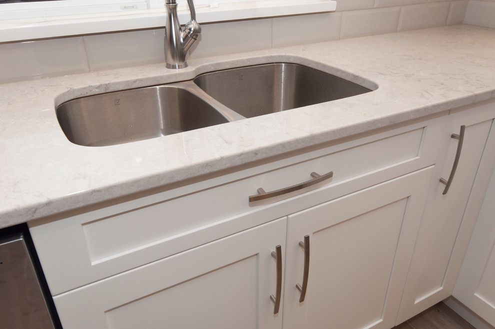 Inspiration for a mid-sized transitional l-shaped light wood floor eat-in kitchen remodel in Vancouver with an undermount sink, shaker cabinets, white cabinets, quartz countertops, white backsplash, ceramic backsplash, stainless steel appliances and an island