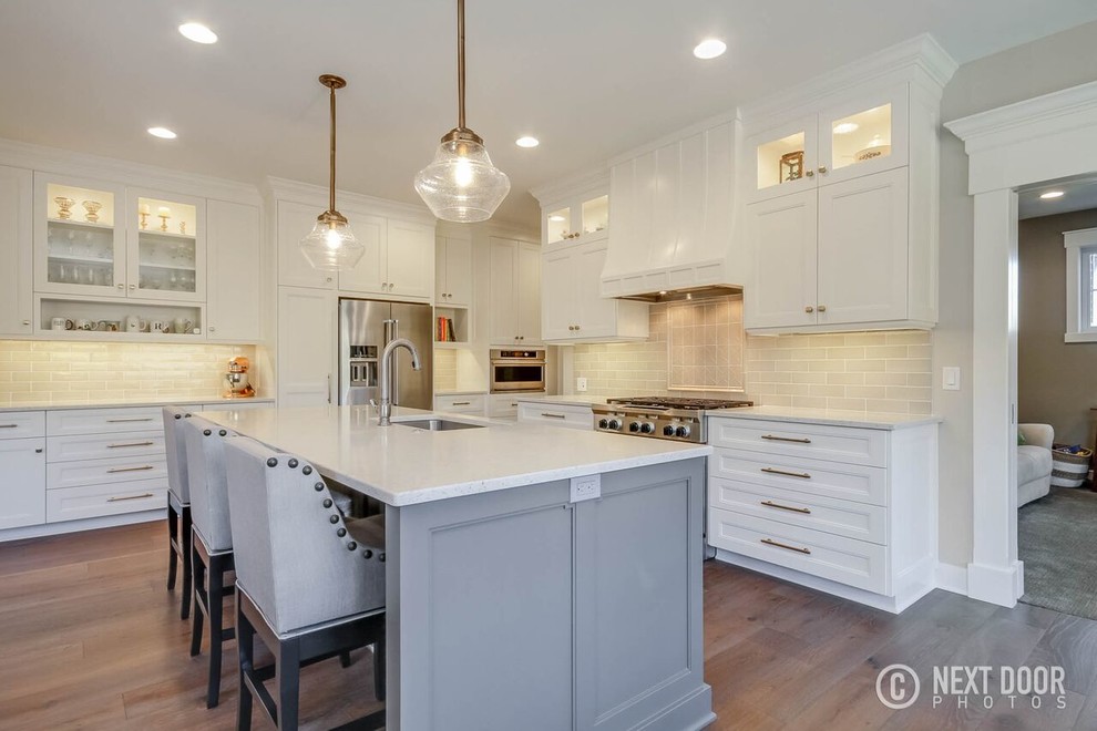 Inspiration for a mid-sized transitional u-shaped open concept kitchen remodel in Grand Rapids with an undermount sink, shaker cabinets, white cabinets, solid surface countertops, beige backsplash, ceramic backsplash and an island