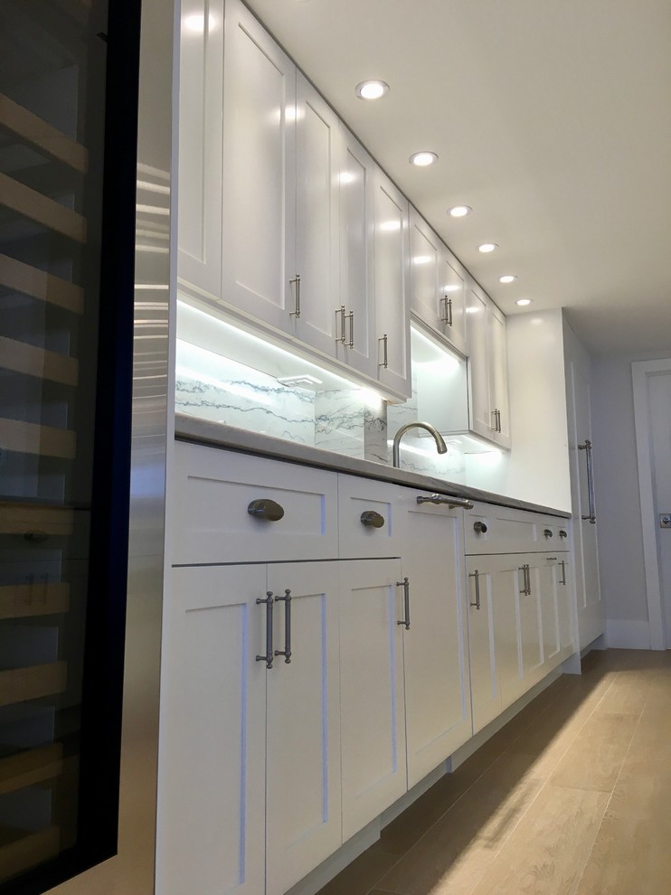 Large transitional galley light wood floor and beige floor open concept kitchen photo in Miami with an undermount sink, shaker cabinets, white cabinets, marble countertops, gray backsplash, marble backsplash, stainless steel appliances and an island