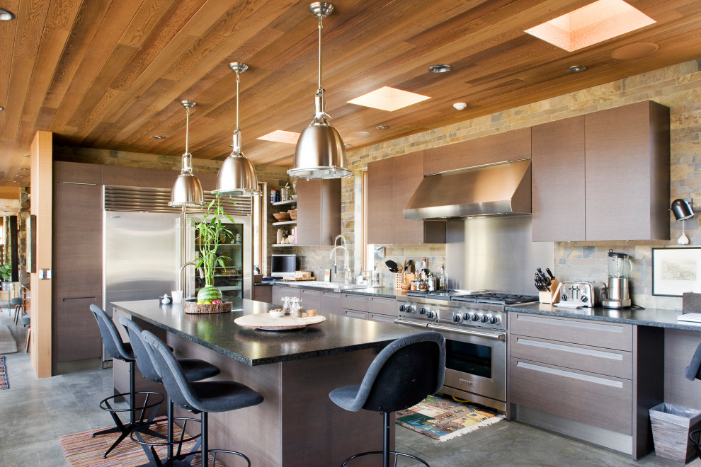 Photo of an expansive modern l-shaped eat-in kitchen in Denver with flat-panel cabinets, dark wood cabinets, brown splashback, stainless steel appliances, with island, grey floor and black benchtop.