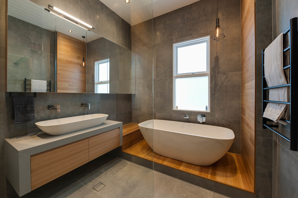 Photo of a large contemporary master bathroom in Brisbane with light wood cabinets, a freestanding tub, gray tile, ceramic tile, grey walls, ceramic floors, engineered quartz benchtops, a trough sink, a corner shower and grey benchtops.