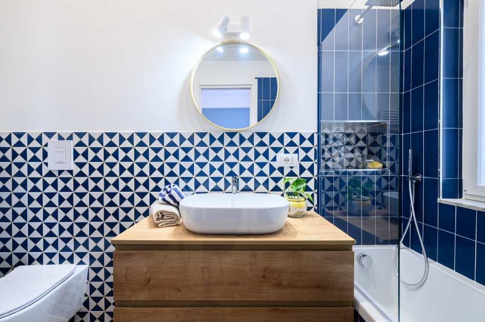 Immagine di una stanza da bagno padronale mediterranea con ante lisce, ante blu, vasca da incasso, WC a due pezzi, piastrelle blu, piastrelle in ceramica, pareti bianche, lavabo a bacinella, top in legno, un lavabo e mobile bagno sospeso