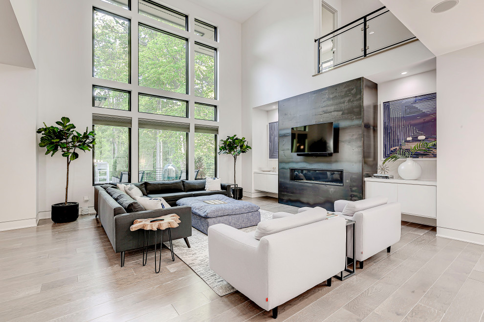 This is an example of a large contemporary open concept living room in Indianapolis with white walls, light hardwood floors, a standard fireplace, a tile fireplace surround, a wall-mounted tv and grey floor.