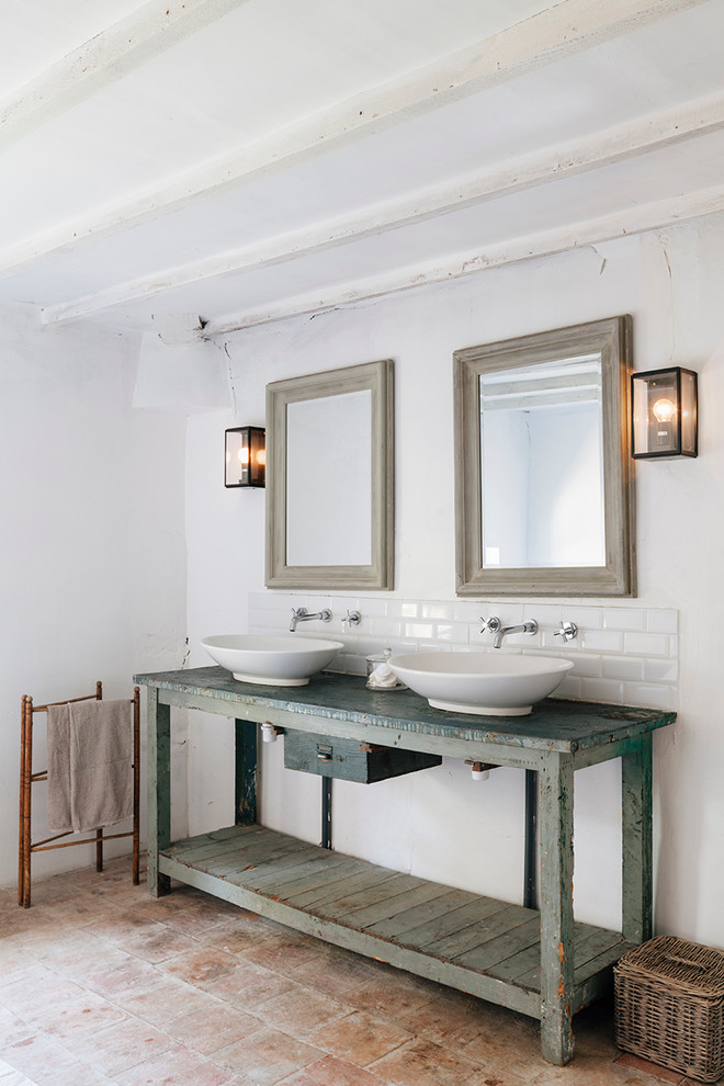 Photo of a mid-sized mediterranean bathroom in Oxfordshire with a vessel sink, distressed cabinets, white tile, subway tile, white walls and terra-cotta floors.