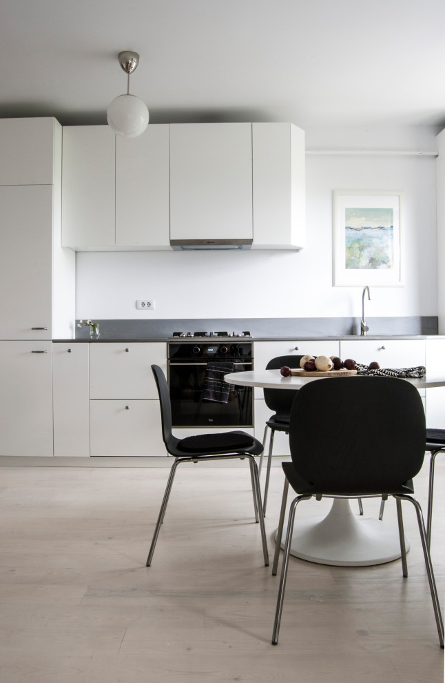 Design ideas for a mid-sized scandinavian single-wall eat-in kitchen in Other with an integrated sink, flat-panel cabinets, white cabinets, wood benchtops, grey splashback, timber splashback, black appliances, painted wood floors, no island, white floor and grey benchtop.