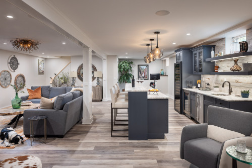 Open concept basement living room with grey shaker kitchen cabinet wall, island seating, and modern lighting.
