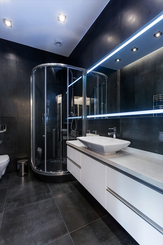 This is an example of a small contemporary 3/4 bathroom in Moscow with flat-panel cabinets, white cabinets, a corner shower, a wall-mount toilet, black tile, porcelain tile, black walls, porcelain floors, a vessel sink, engineered quartz benchtops, black floor, a sliding shower screen and white benchtops.