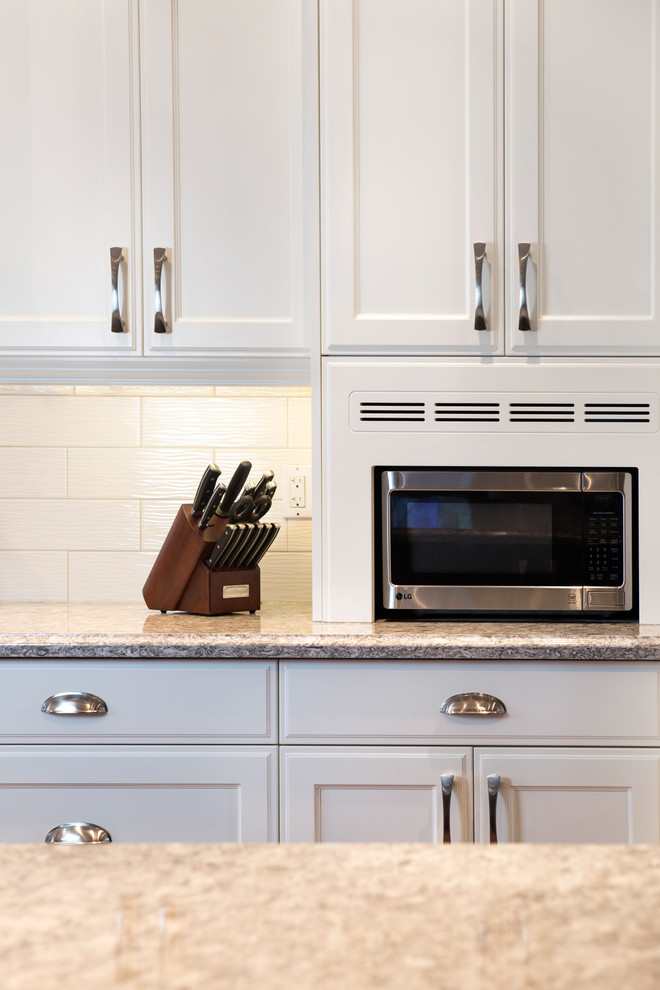 Inspiration for a large transitional l-shaped medium tone wood floor kitchen remodel in Toronto with an undermount sink, recessed-panel cabinets, white cabinets, quartz countertops, white backsplash, subway tile backsplash, stainless steel appliances and an island