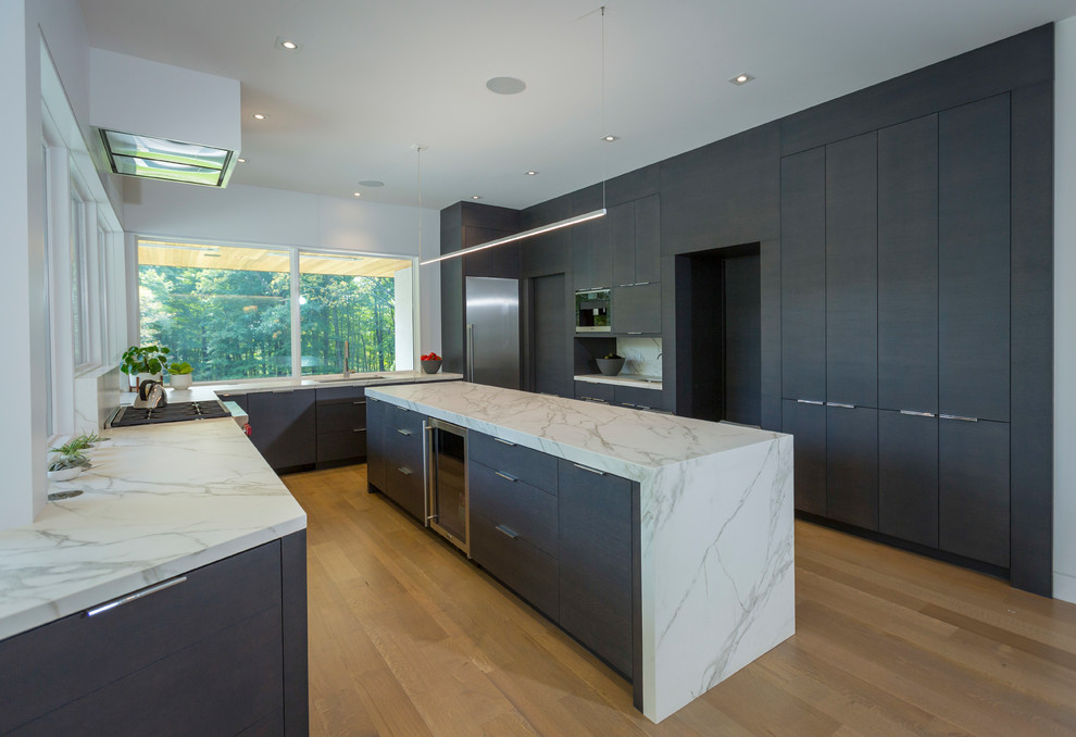 Photo of a large contemporary u-shaped eat-in kitchen in Cincinnati with a drop-in sink, flat-panel cabinets, black cabinets, onyx benchtops, stainless steel appliances, light hardwood floors, with island, beige floor and multi-coloured benchtop.