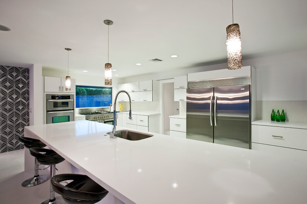 Photo of an expansive midcentury l-shaped open plan kitchen in Other with an undermount sink, flat-panel cabinets, white cabinets, quartz benchtops, white splashback, porcelain splashback, stainless steel appliances, porcelain floors and with island.