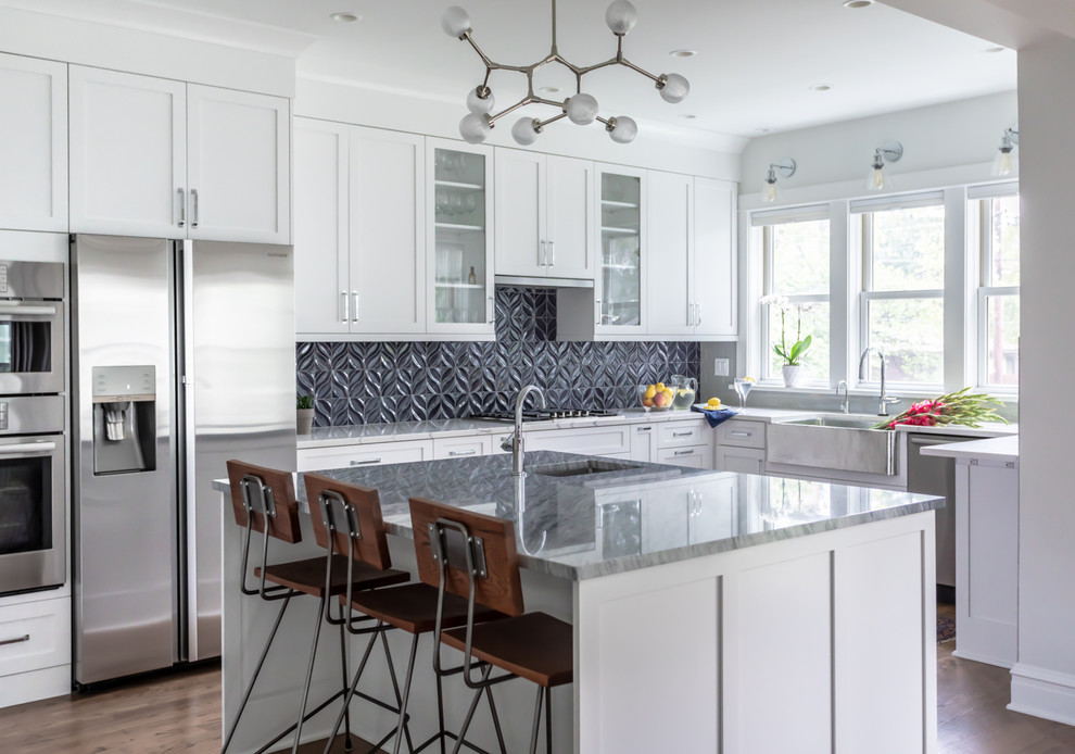 Transitional u-shaped dark wood floor and brown floor kitchen photo in Chicago with a farmhouse sink, shaker cabinets, white cabinets, black backsplash, stainless steel appliances, an island and white countertops