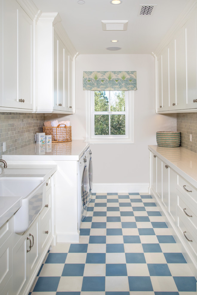 Large transitional galley dedicated laundry room in Orange County with a farmhouse sink, shaker cabinets, white cabinets, a side-by-side washer and dryer, quartz benchtops, ceramic floors, multi-coloured floor, white benchtop and grey walls.