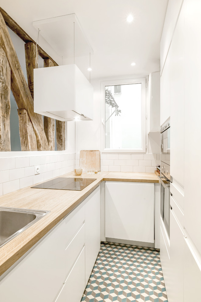 This is an example of a mid-sized scandinavian u-shaped separate kitchen in Paris with a drop-in sink, flat-panel cabinets, white cabinets, wood benchtops, white splashback, subway tile splashback, stainless steel appliances, no island, cement tiles, multi-coloured floor and beige benchtop.