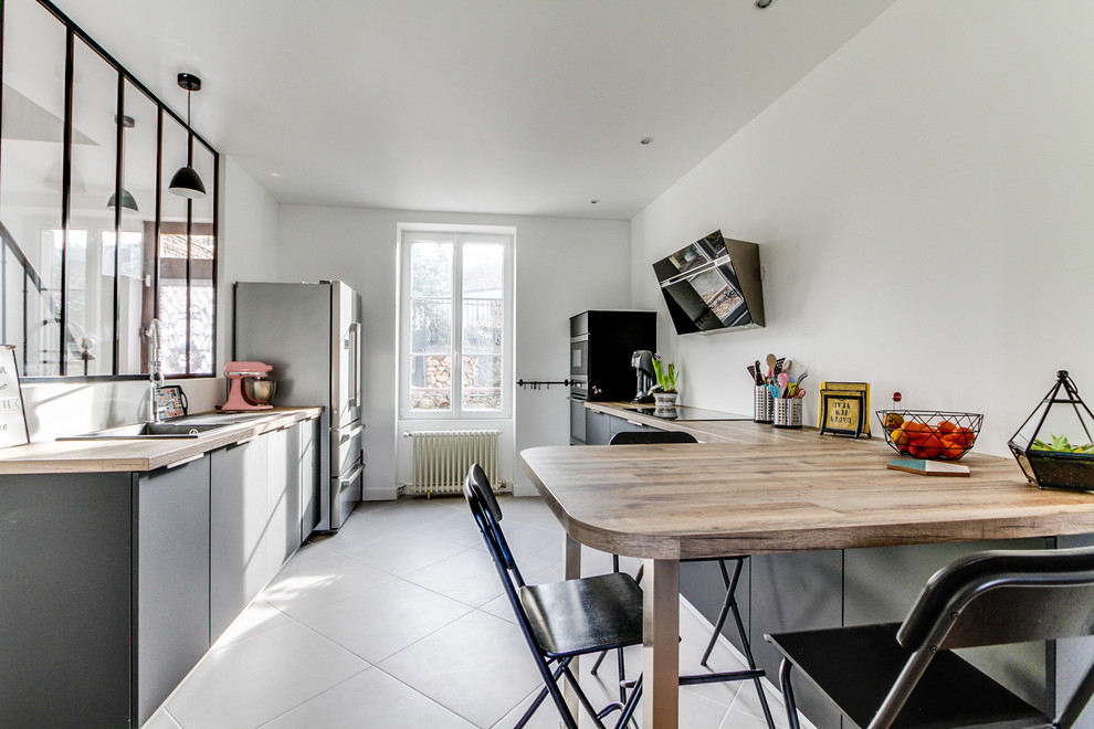 Large scandinavian eat-in kitchen in Paris with an undermount sink, beaded inset cabinets, grey cabinets, black appliances, ceramic floors, grey floor, beige benchtop, laminate benchtops and a peninsula.