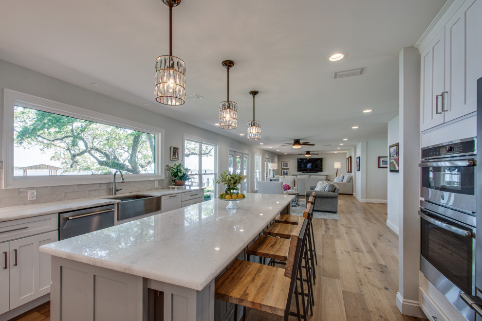 Large transitional u-shaped kitchen in Other with a farmhouse sink, recessed-panel cabinets, white cabinets, white splashback, shiplap splashback, stainless steel appliances, with island, beige floor and white benchtop.
