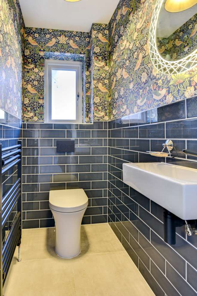 Inspiration for a small eclectic cloakroom in Sussex with a wall mounted toilet, blue tiles, ceramic tiles, multi-coloured walls, porcelain flooring, a wall-mounted sink, grey floors, feature lighting and wallpapered walls.