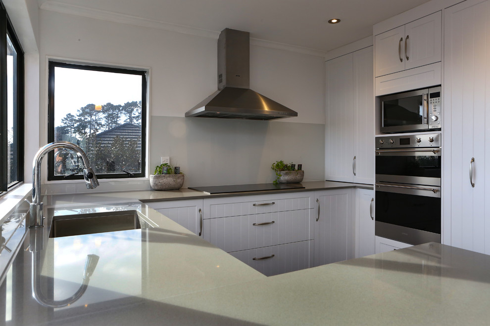Inspiration for a mid-sized country u-shaped open plan kitchen in Auckland with an undermount sink, shaker cabinets, white cabinets, quartz benchtops, grey splashback, glass sheet splashback, stainless steel appliances, a peninsula and grey benchtop.