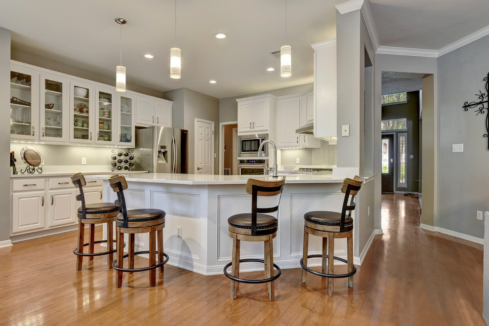 Example of a mid-sized transitional u-shaped light wood floor eat-in kitchen design in Austin with an undermount sink, white cabinets, quartz countertops, white backsplash, stone slab backsplash, stainless steel appliances, a peninsula and raised-panel cabinets