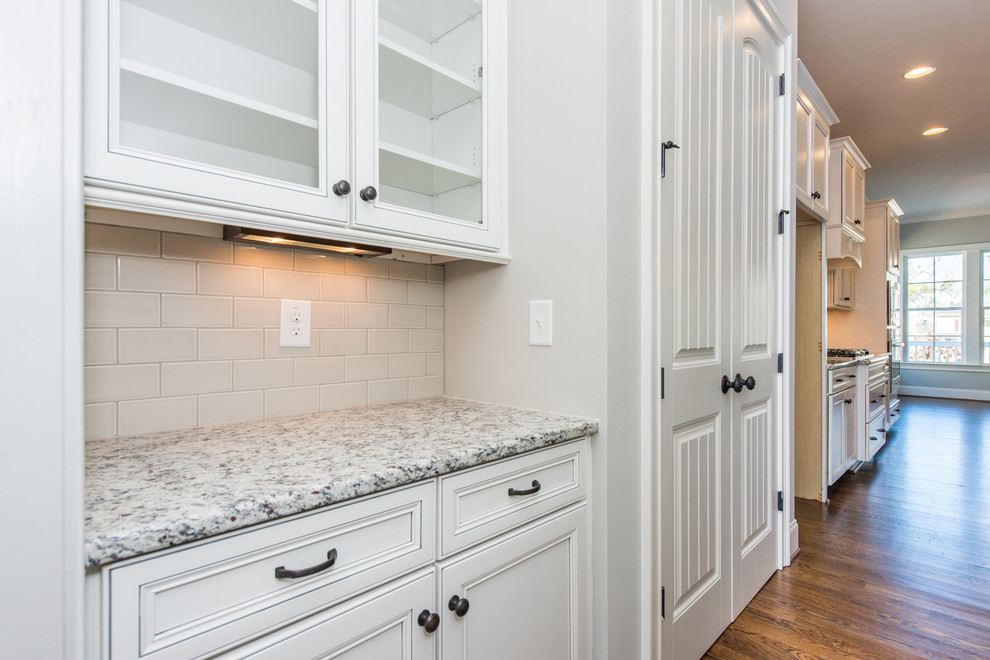 Inspiration for a traditional kitchen in Raleigh with flat-panel cabinets, white cabinets, granite benchtops, white splashback, ceramic splashback, stainless steel appliances and medium hardwood floors.