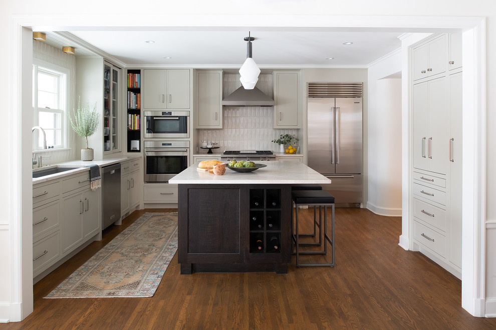 This is an example of a transitional l-shaped kitchen in Minneapolis with an undermount sink, recessed-panel cabinets, grey cabinets, grey splashback, stainless steel appliances, dark hardwood floors, with island, brown floor and white benchtop.