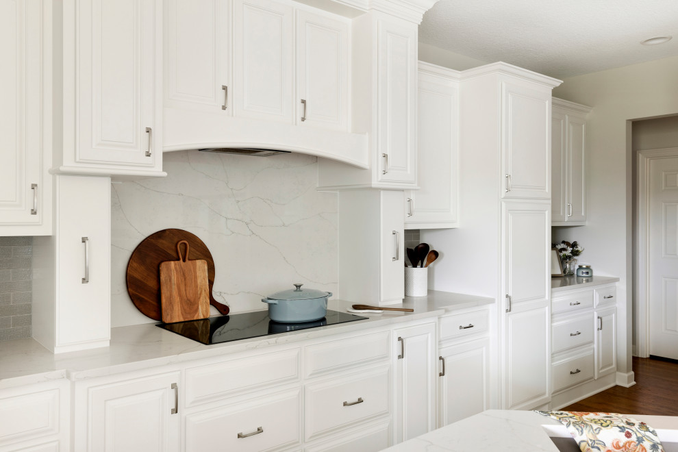 Inredning av ett klassiskt mellanstort vit vitt kök, med en undermonterad diskho, luckor med upphöjd panel, vita skåp, bänkskiva i kvartsit, grått stänkskydd, stänkskydd i glaskakel, rostfria vitvaror, mörkt trägolv, en köksö och brunt golv