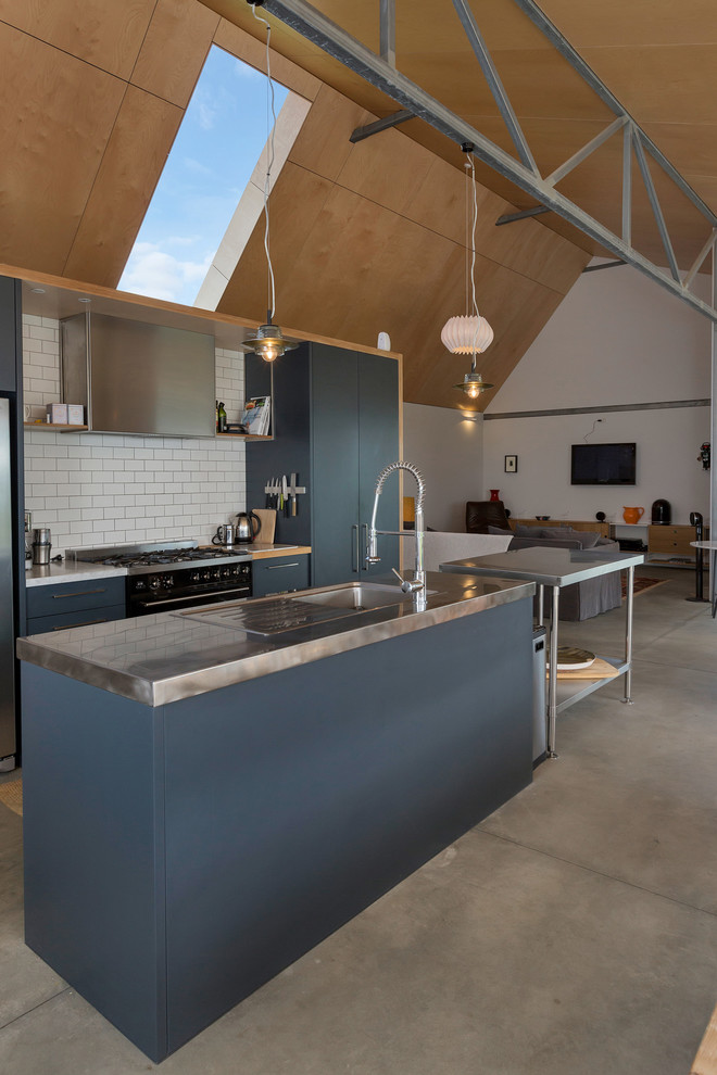This is an example of a large contemporary single-wall open plan kitchen in Auckland with a drop-in sink, flat-panel cabinets, blue cabinets, stainless steel benchtops, subway tile splashback, stainless steel appliances, concrete floors, with island and grey floor.