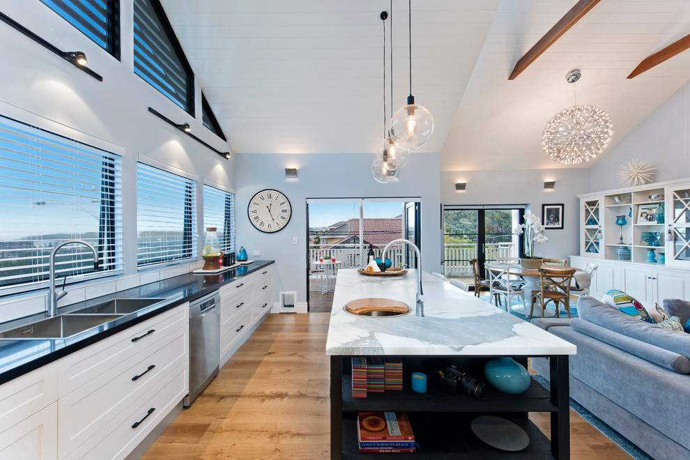 Inspiration for a beach style galley open plan kitchen in Sydney with a double-bowl sink, shaker cabinets, white cabinets, wood benchtops, white splashback, stainless steel appliances, light hardwood floors and with island.