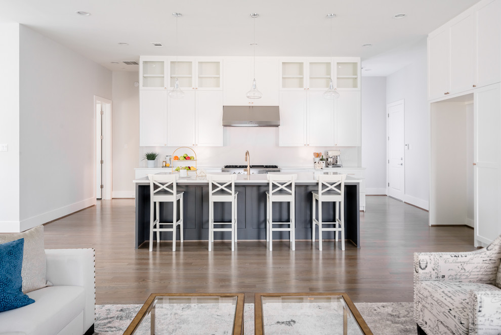 Open concept kitchen - transitional single-wall medium tone wood floor and brown floor open concept kitchen idea in Houston with a farmhouse sink, shaker cabinets, white cabinets, quartzite countertops, white backsplash, porcelain backsplash, stainless steel appliances, an island and white countertops