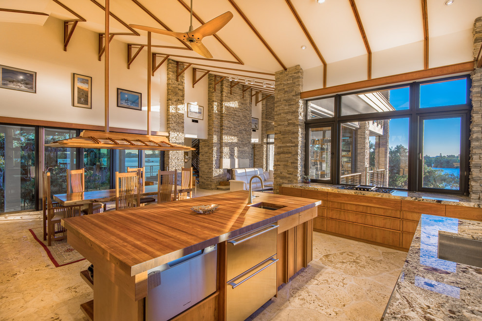 This is an example of a large midcentury l-shaped open plan kitchen in Tampa with an undermount sink, flat-panel cabinets, medium wood cabinets, wood benchtops, panelled appliances, limestone floors and with island.
