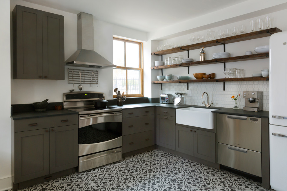This is an example of a mid-sized eclectic l-shaped eat-in kitchen in Philadelphia with a farmhouse sink, flat-panel cabinets, grey cabinets, white splashback, ceramic splashback, stainless steel appliances, porcelain floors, no island and multi-coloured floor.