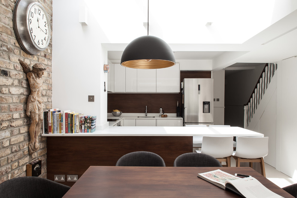 Design ideas for a contemporary u-shaped eat-in kitchen in London with an undermount sink, flat-panel cabinets, white cabinets, brown splashback, stainless steel appliances and a peninsula.