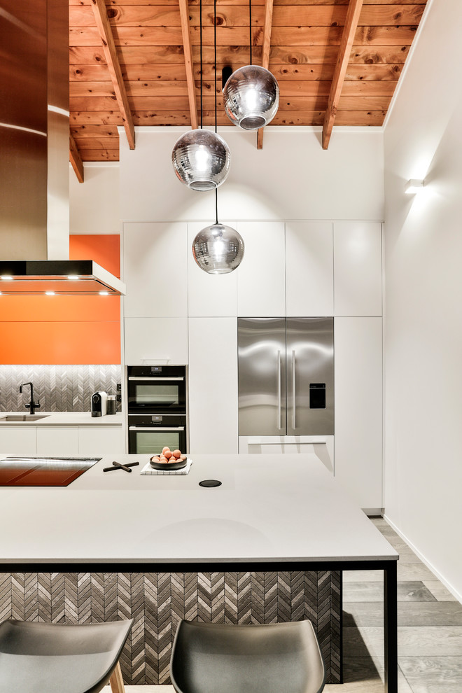 Photo of a mid-sized modern galley eat-in kitchen in Auckland with a single-bowl sink, flat-panel cabinets, orange cabinets, quartz benchtops, black splashback, porcelain splashback, black appliances, painted wood floors, with island, grey floor and grey benchtop.