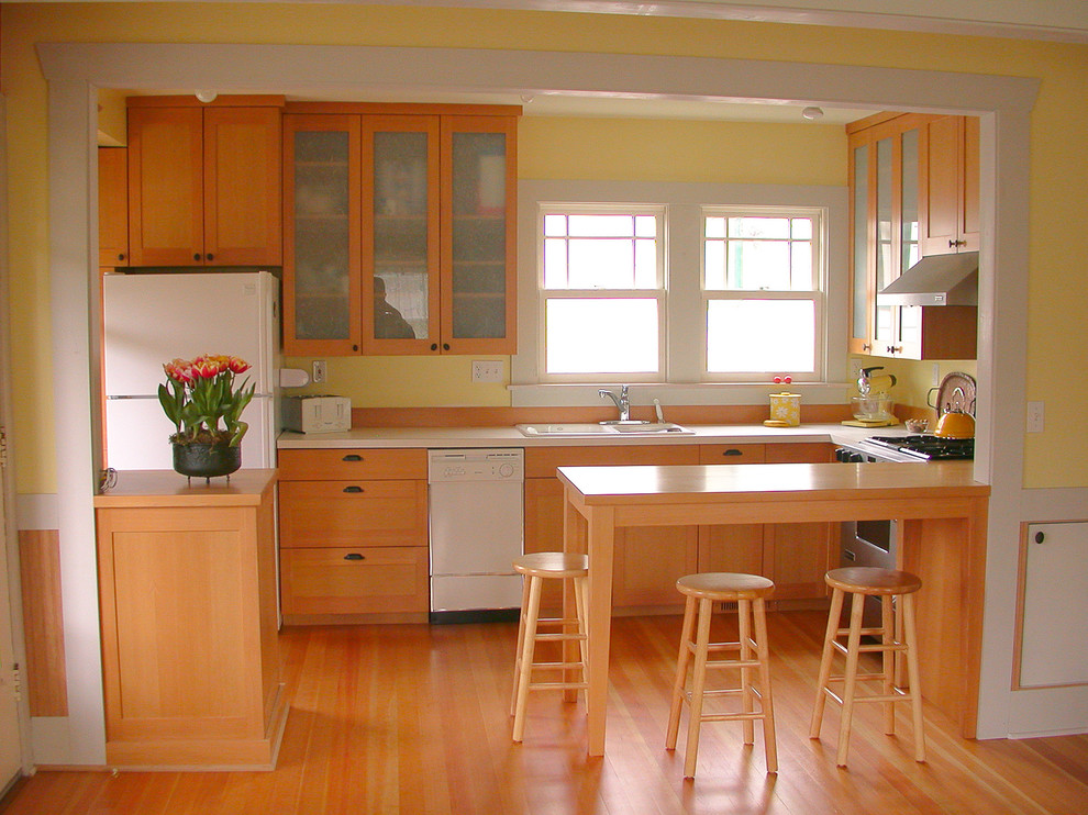 Inspiration for a mid-sized traditional u-shaped eat-in kitchen in Seattle with a double-bowl sink, shaker cabinets, light wood cabinets, solid surface benchtops, yellow splashback, white appliances, light hardwood floors and a peninsula.