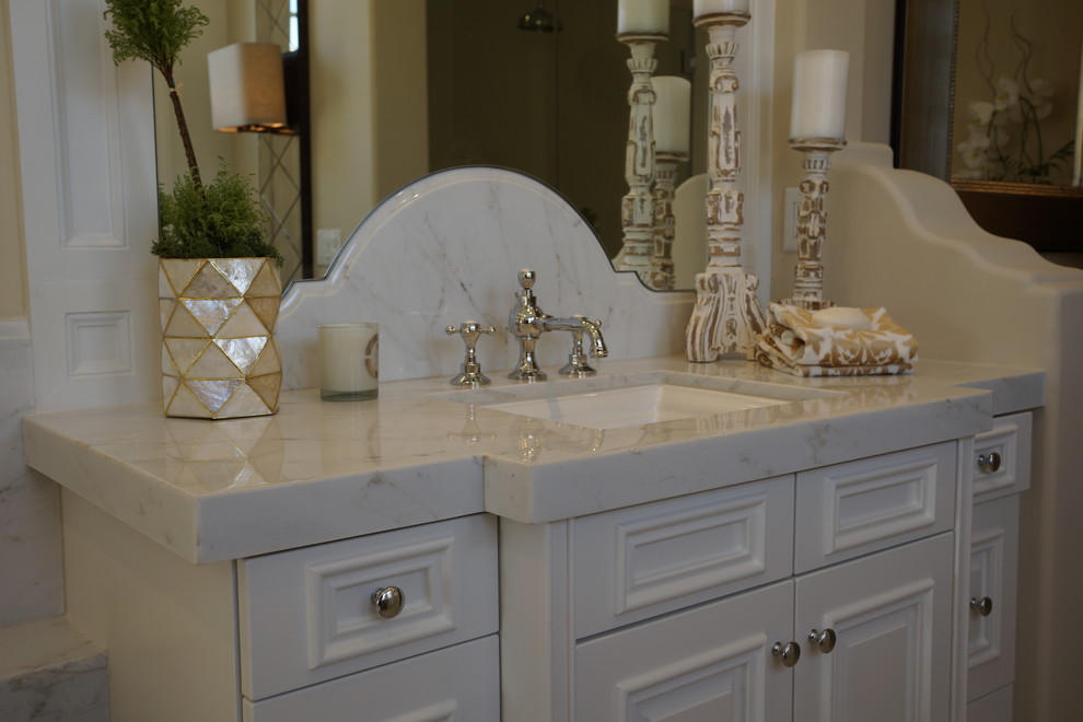 Design ideas for a large mediterranean master bathroom in San Diego with an undermount sink, raised-panel cabinets, white cabinets, granite benchtops, a freestanding tub, beige walls and marble floors.