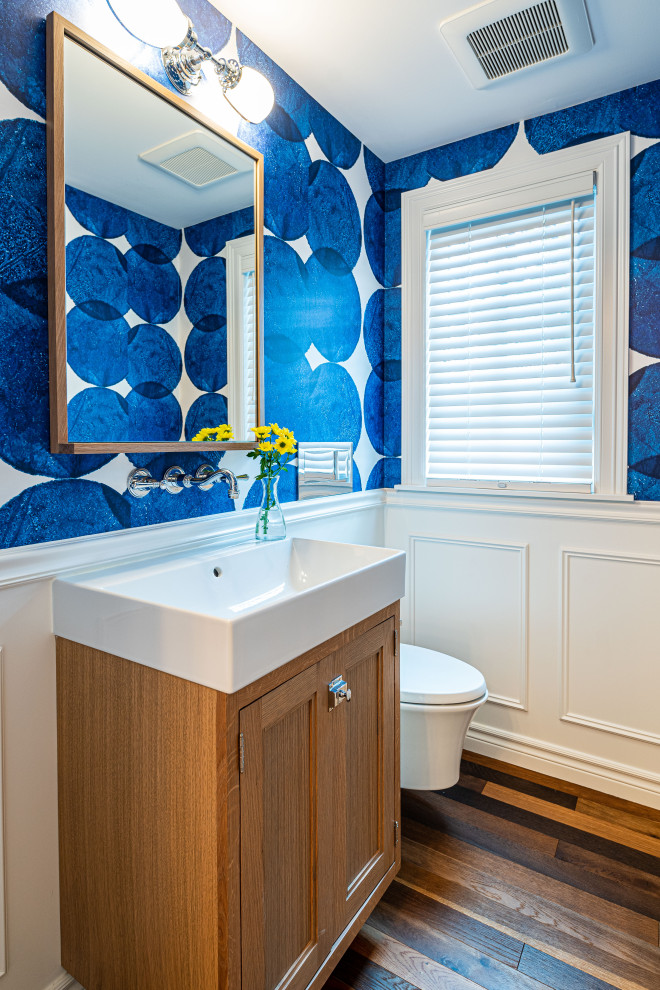 Cette photo montre un WC suspendu moderne en bois vieilli avec un placard à porte affleurante, un carrelage blanc, un mur bleu, un sol en bois brun, un lavabo intégré, un sol marron, un plan de toilette blanc, meuble-lavabo sur pied et du papier peint.