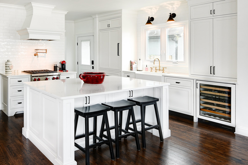 Photo of a large transitional l-shaped eat-in kitchen in Jacksonville with a farmhouse sink, white cabinets, quartz benchtops, white splashback, ceramic splashback, dark hardwood floors, with island, shaker cabinets, brown floor, panelled appliances and white benchtop.